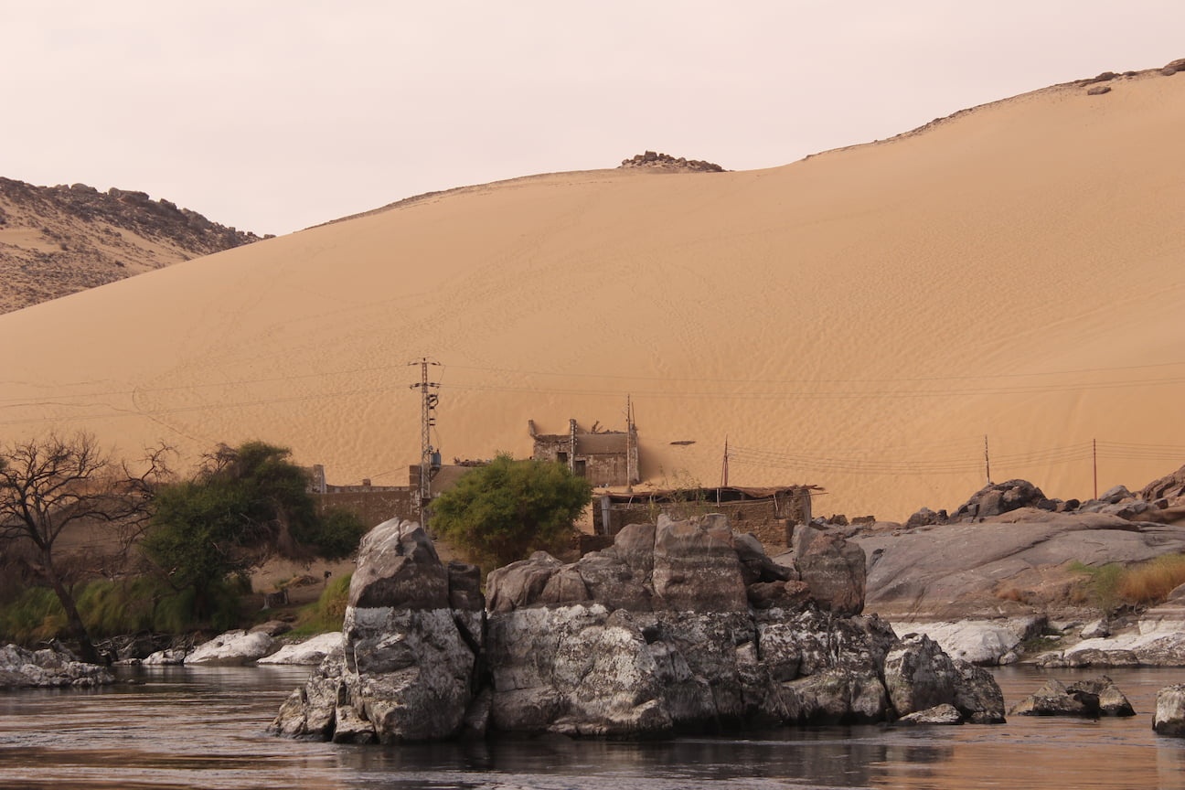 River bank on the Nile, showing the ruins of a house partially covered by the sand dune