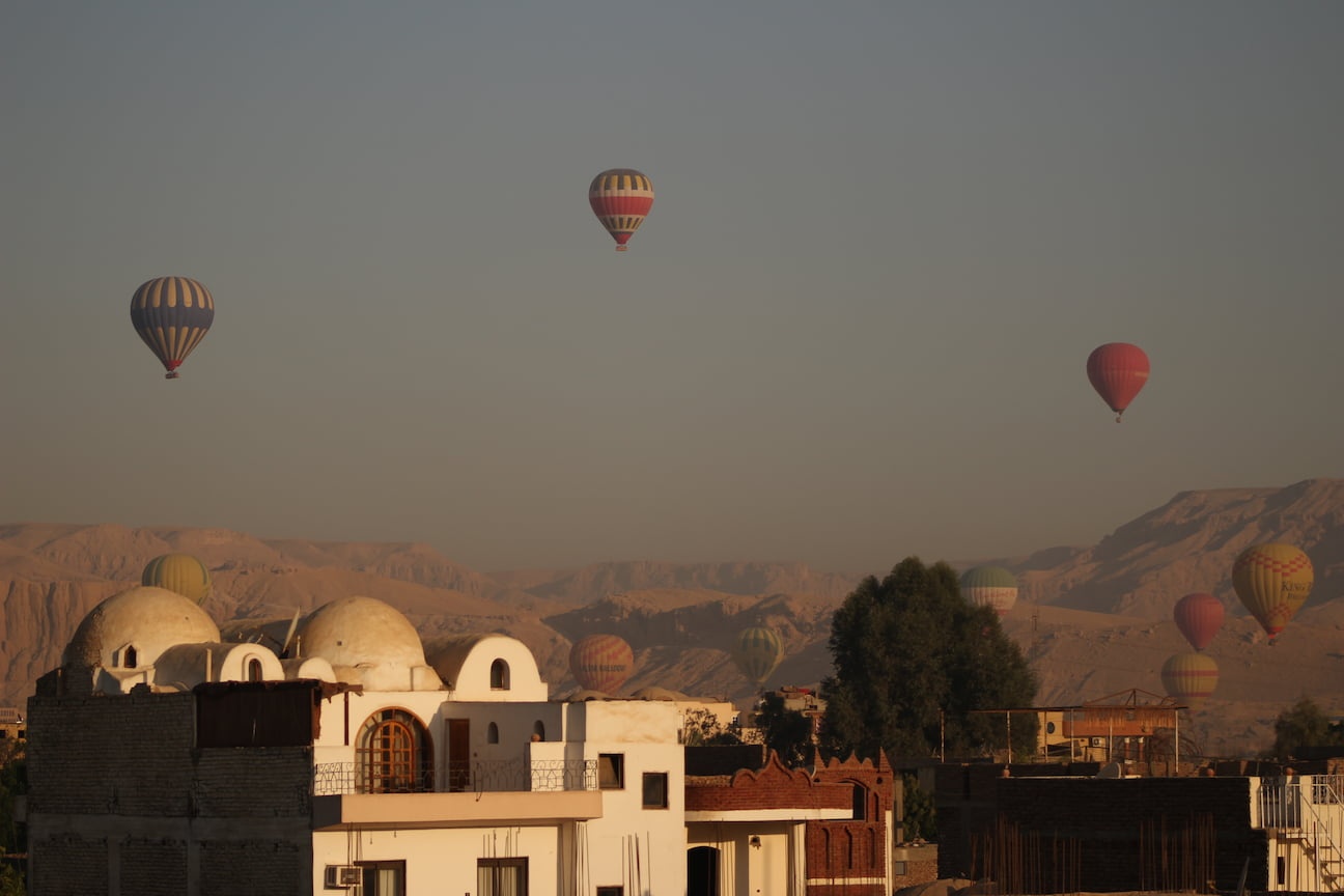 Several hot air balloons flying over houses and the Valley of the Kings, in Luxor