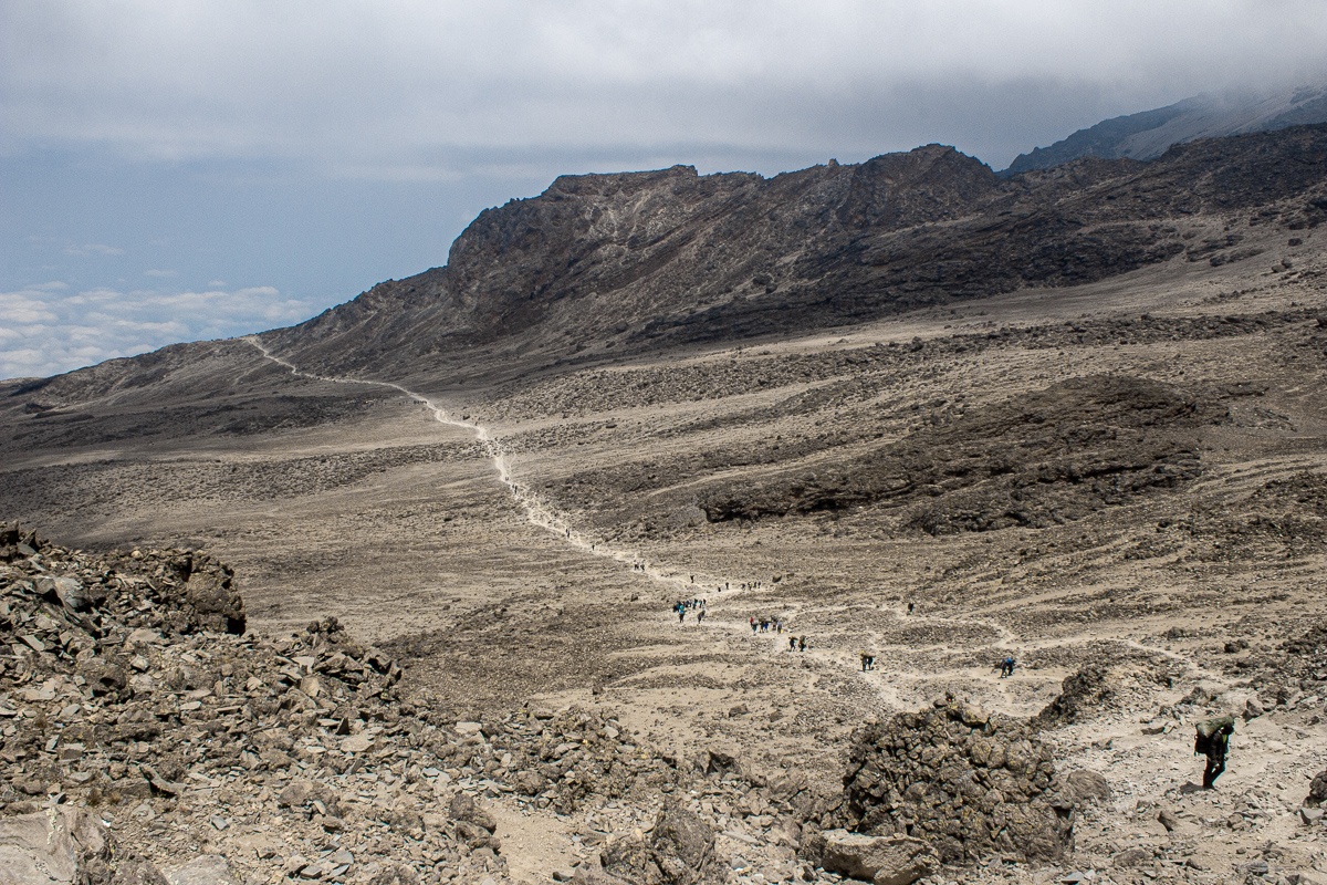 A few hikers and porters walking up the path through the barren landscape