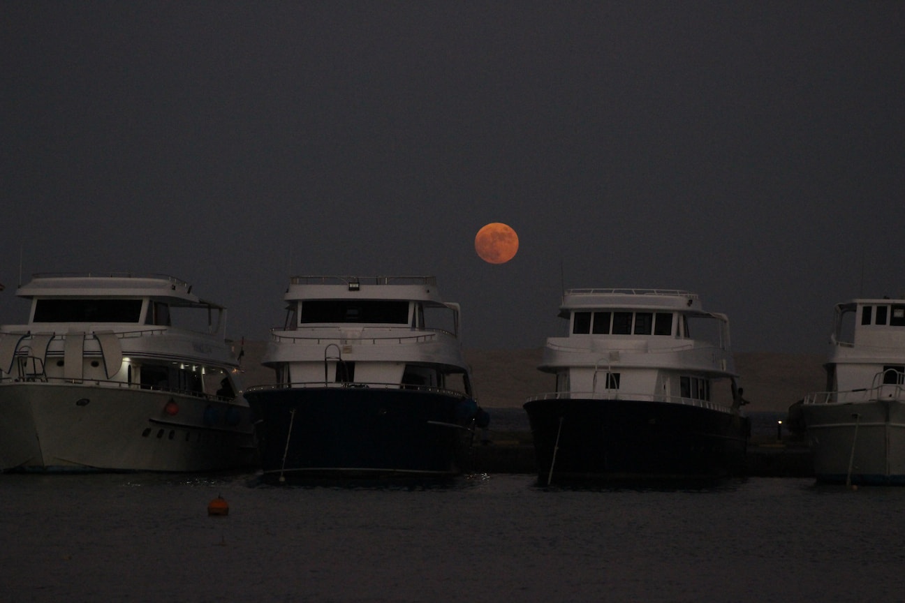 Red moon can be seen between four boats in the marina, Hurghada