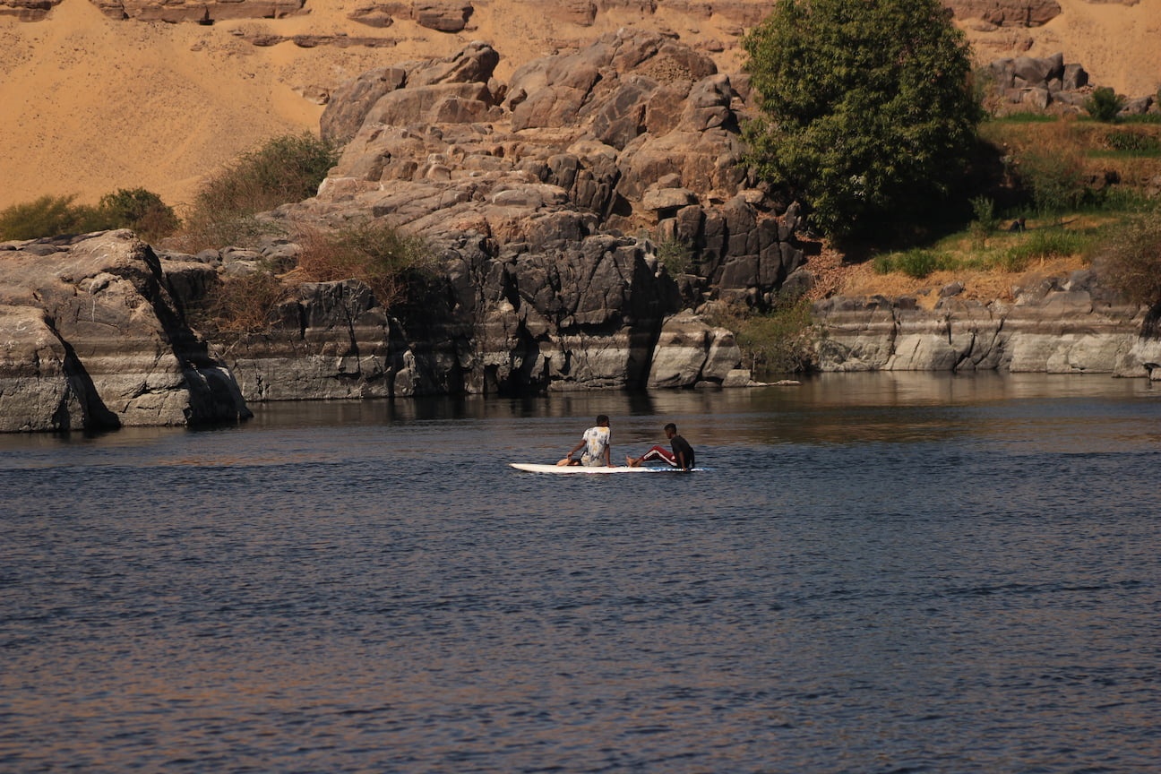 Two kids on a surf board using their hands to paddle through the Nile waters