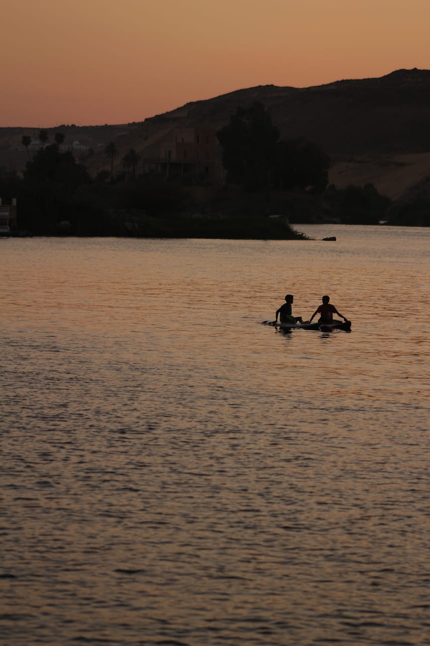 Two kids on a surf board using their hands to paddle through the Nile waters at night