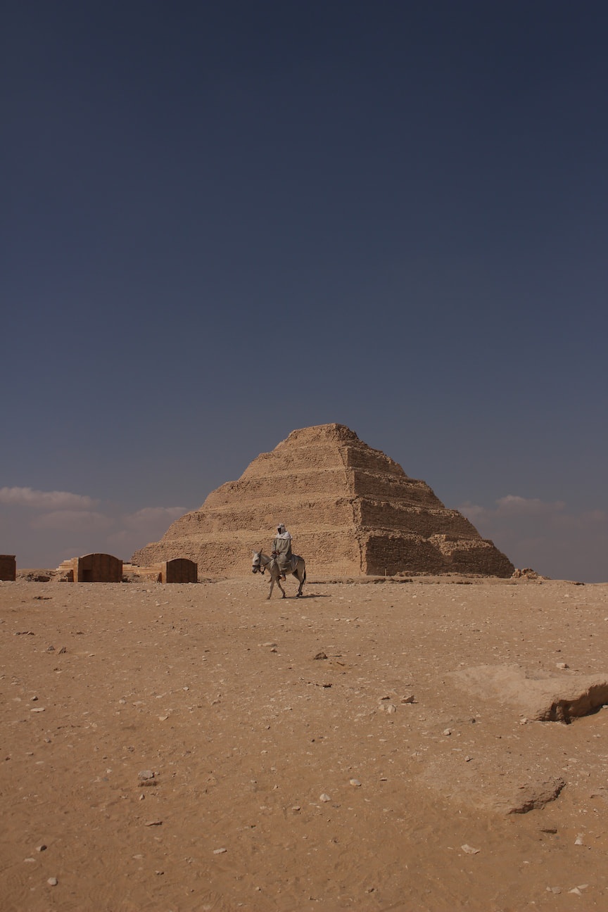 A man rides a donkey, with Djoser Pyramid on the background